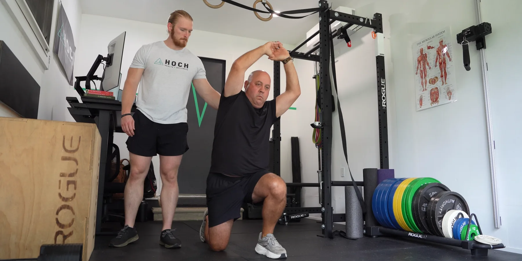 A Hoch Health coach guiding a client through a half-kneeling get-up movement in the gym